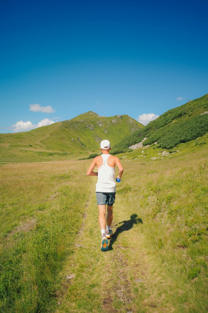 Back view of a man running on a sunny mountain trail, exemplifying outdoor fitness.